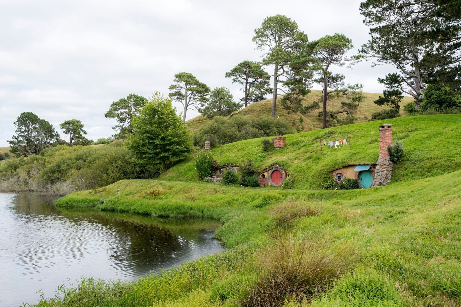 Hobbit-holes beside a lake at a green rural film-set landscape, New Zealand