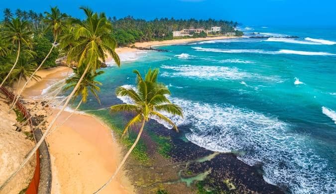 Aerial view of a palm-fringed turquoise beach on the southern coast of Sri Lanka