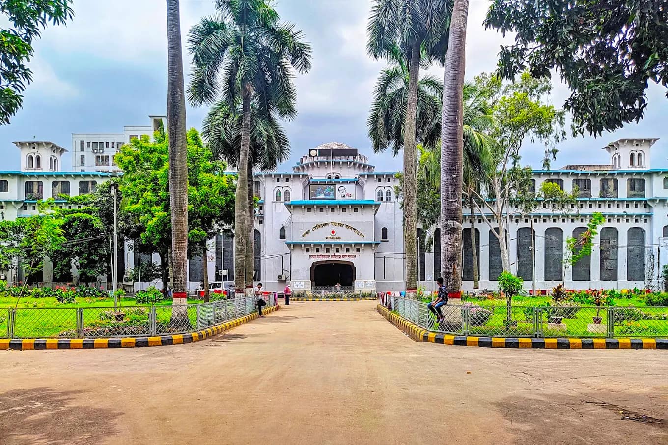 Main academic building of Dhaka Medical College behind a palm-lined driveway
