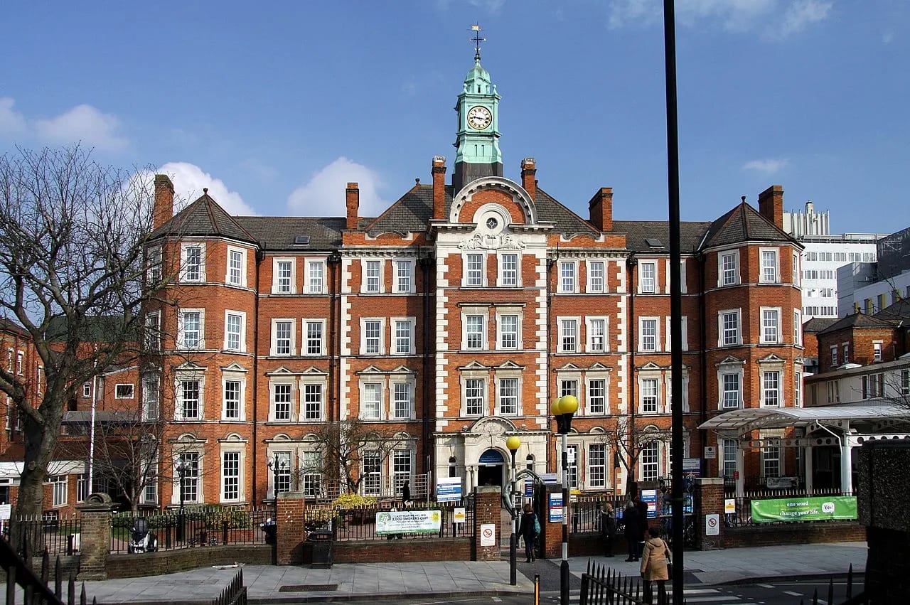 A historic red-brick Imperial College teaching hospital building with a green clock tower in London