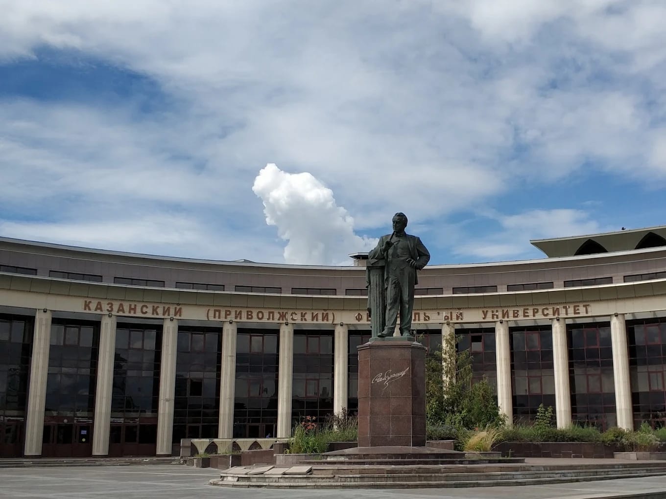 A curved modern Kazan Federal University building with Russian signage and a statue outside
