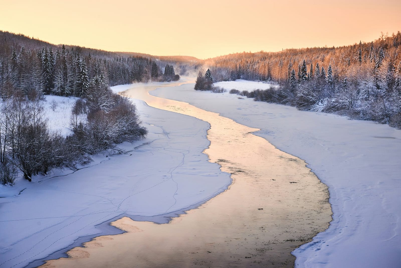 A partly frozen Russian river winding through snow-covered pine forest at sunrise