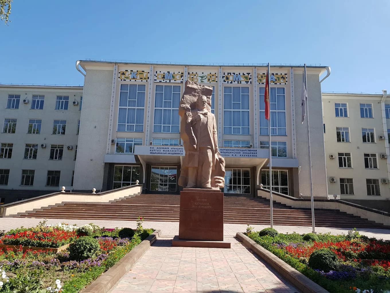 Daytime view of the Kyrgyz State Medical Academy main building with the Akhunbaev monument and flags