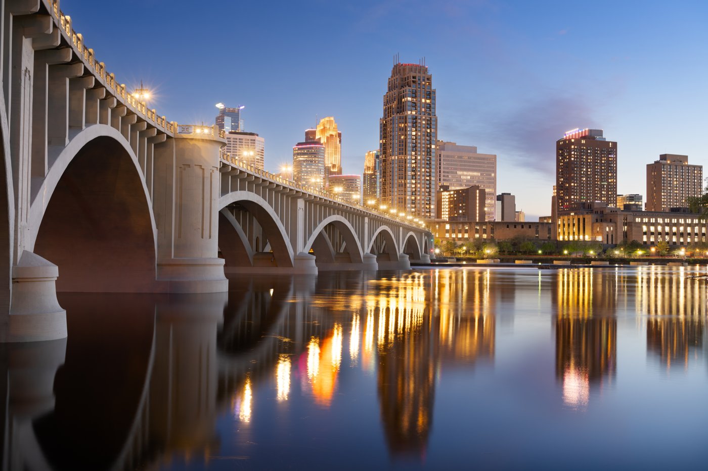 A historic stone arch bridge and a Minnesota city skyline at dusk