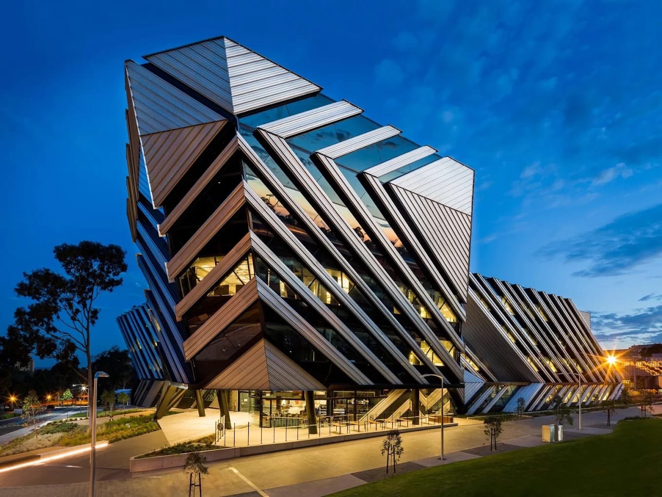 An angular, diamond-facade Monash research building illuminated at dusk on the Clayton campus, Melbourne