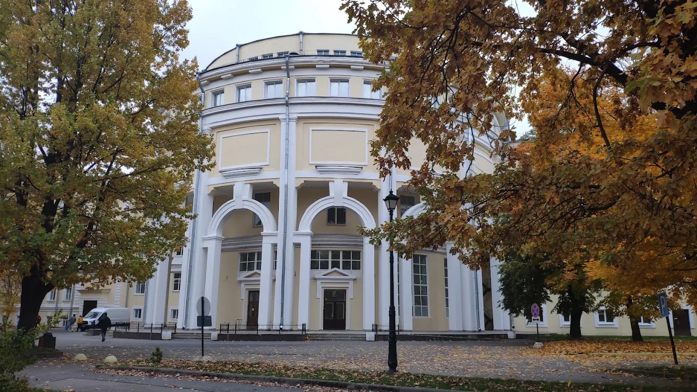 A cream-coloured neoclassical rotunda building with columns on the Pavlov University campus in St Petersburg, framed by autumn trees