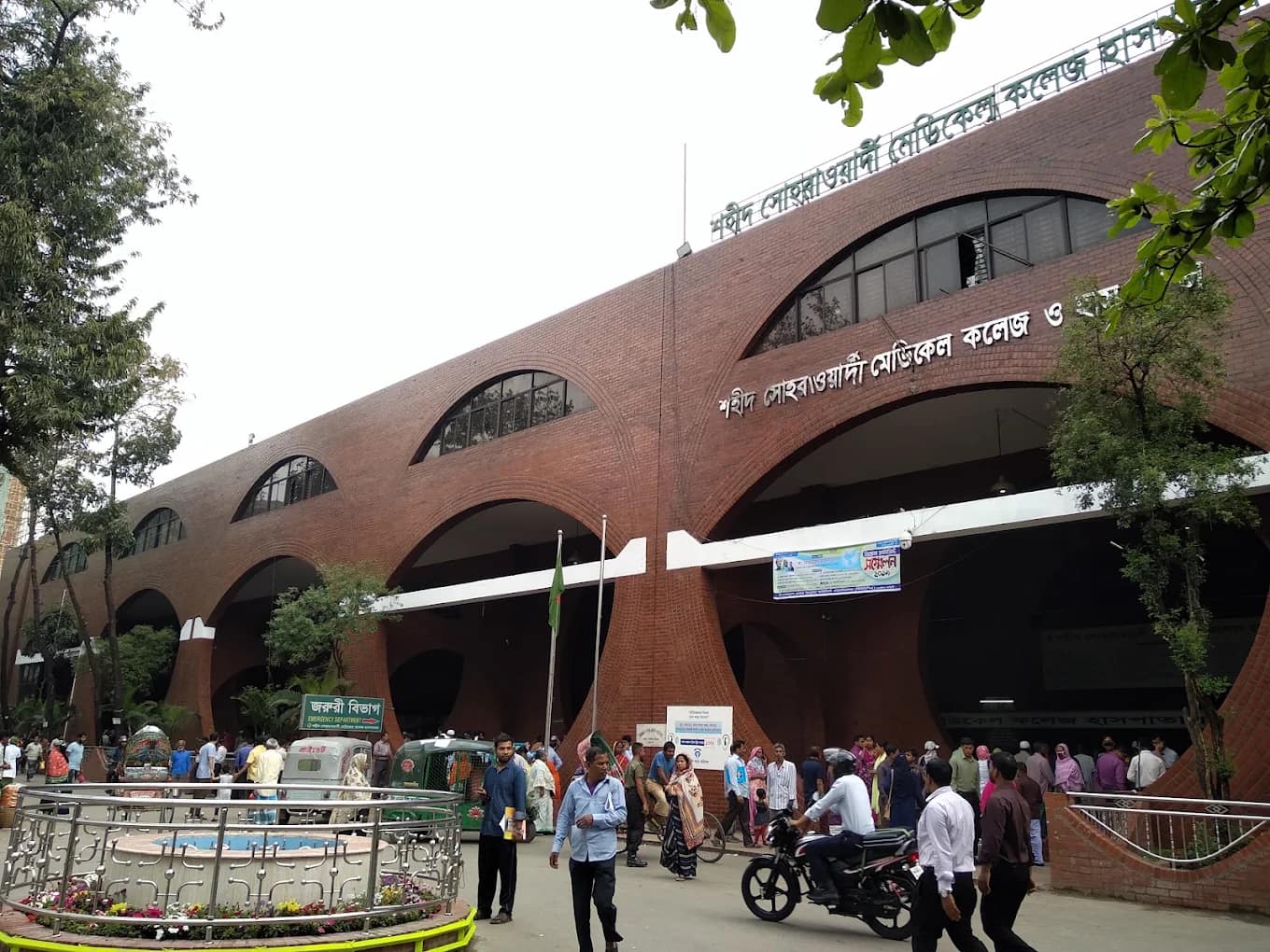 Arched brick facade of Shaheed Suhrawardy Medical College Hospital with patients and visitors outside