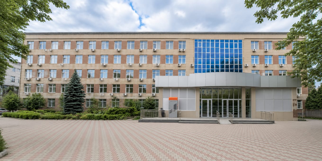 The main academic building of South Kazakhstan Medical Academy in Shymkent, its brick facade fronted by a glass atrium entrance and a paved forecourt