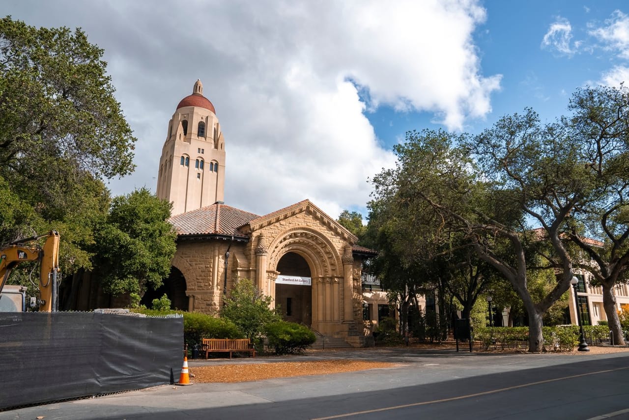 Hoover Tower beside a sandstone arched building at Stanford University