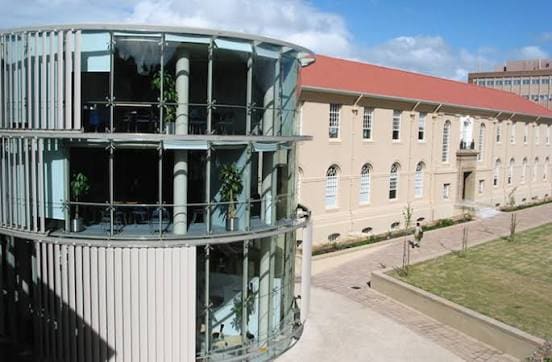 The glass rotunda block of the University of Cape Town health-sciences campus beside a sandstone teaching building