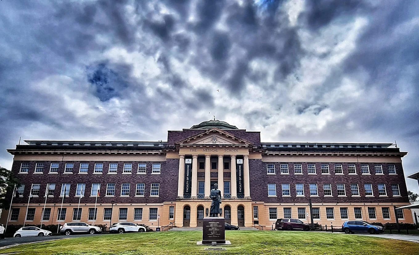 The Mayne Medical School building at the University of Queensland head-on, with 'Faculty of Medicine' banners and a Hippocrates statue in front, Herston, Brisbane