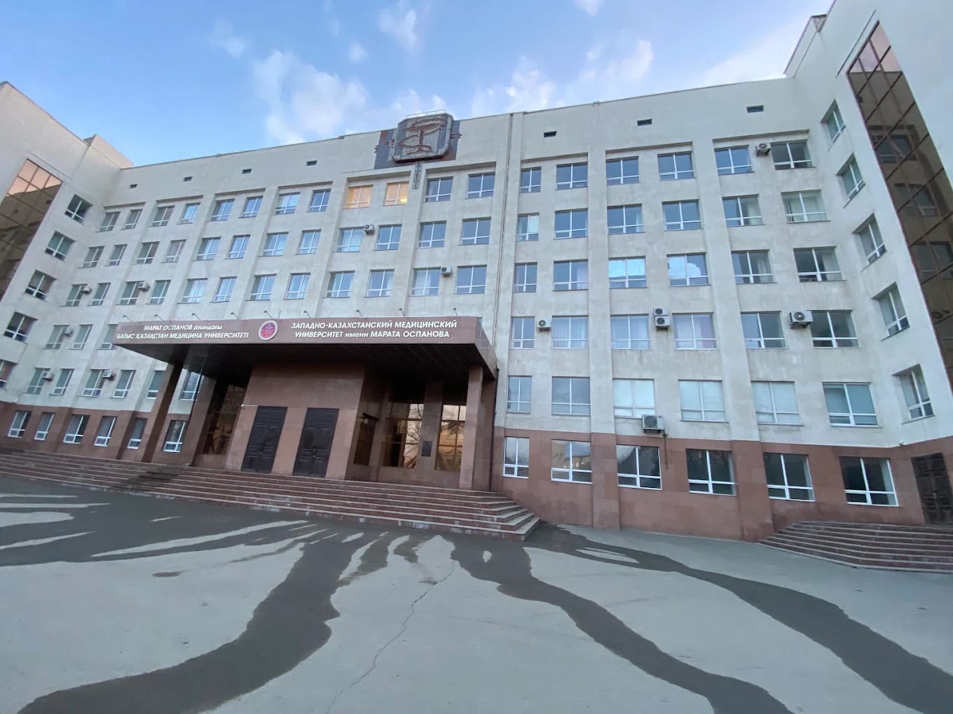 The main building of West Kazakhstan Marat Ospanov Medical University under a blue sky, with its Kazakh and Russian signage, Aktobe
