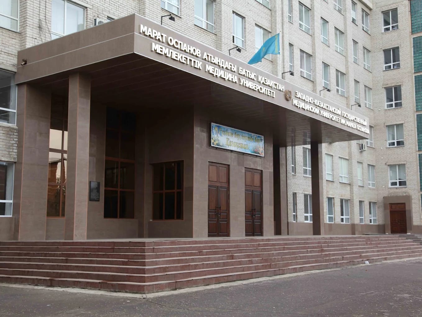 The entrance portico of West Kazakhstan Marat Ospanov Medical University, with the Kazakh flag and Kazakh and Russian signage, Aktobe