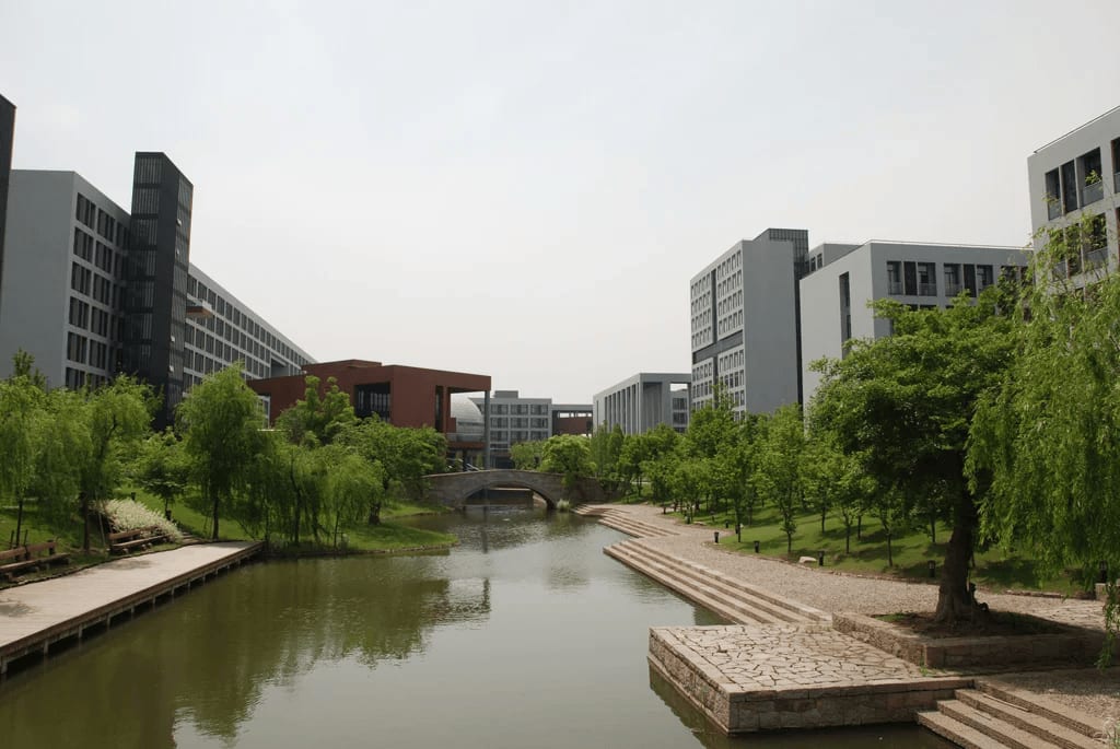 A scenic view of the Zhejiang University campus with a canal, bridge and modern buildings