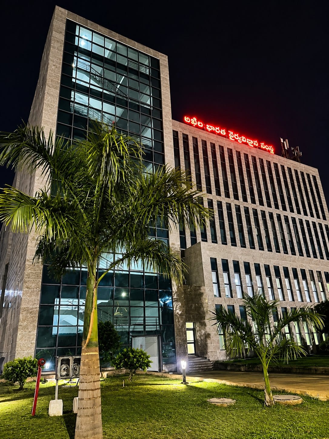 The AIIMS Mangalagiri main building at night, with the institute name board